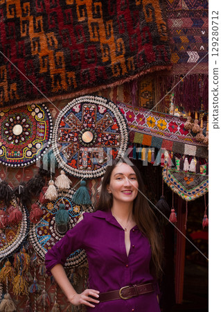 a beautiful girl in dress in a traditional turkish interior with many carpets on the wall 129280712