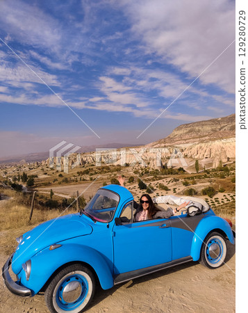 beautiful happy girl in a skirt posing near a retro car in the mountains of cappadocia 129280729