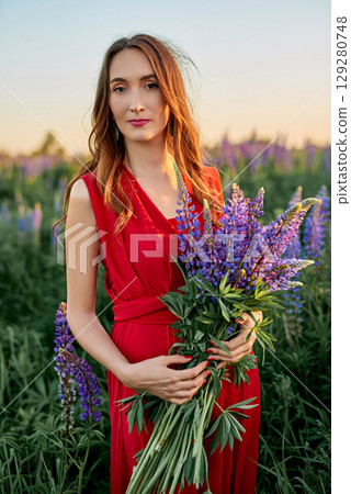 beautiful girl in a red dress with a bouquet of lupine flowers in the field 129280748