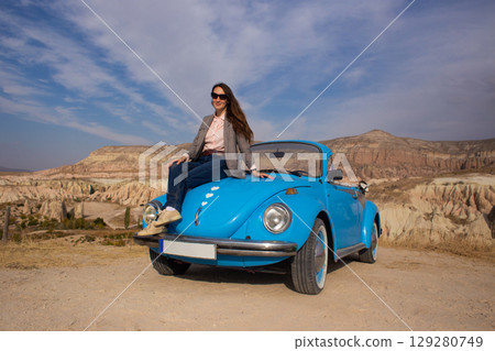 beautiful happy girl in a skirt posing near a retro car in the mountains of cappadocia 129280749