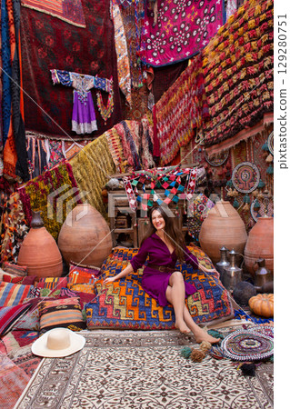 a beautiful girl in dress in a traditional turkish interior with many carpets on the wall 129280751