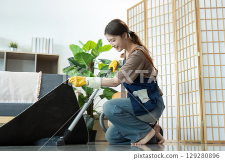 Home Cleaning. Young woman vacuuming carpet with a smile. 129280896