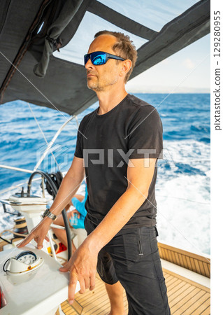 Man standing in the cockpit of a sailing yacht near Croatia, observing the sea and sails during navigation. Freedom, awareness and connection with the moment at sea. 129280955