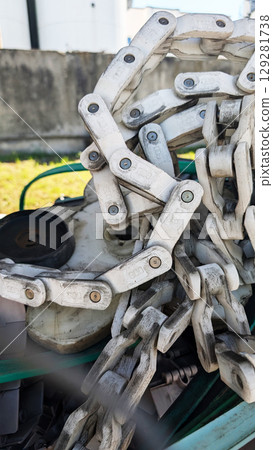 Close-up view of a heavy-duty metal chain resting on machinery, showcasing intricate links and textures, with green machinery components in the background, emphasizing industrial strength and durabili 129281738