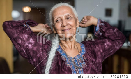 Elderly woman with long white hair is smiling and stretching her arms in a cozy indoor setting, radiating joy and contentment in her expression Elderly woman with long white hair is smiling and stretching her arms in a cozy indoor setting, radiating joy and contentment in her expression 129281810