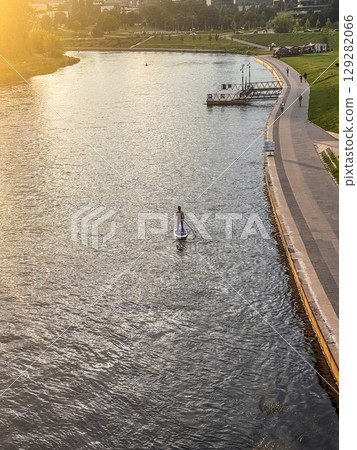 Tranquil urban sunset moment with lone paddleboarder on river path. High quality photo 129282066