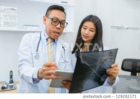 doctor and  nurse are looking at  medical image of  patient's spine 129282171