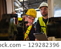 Two men in safety gear looking at a machine 129282396