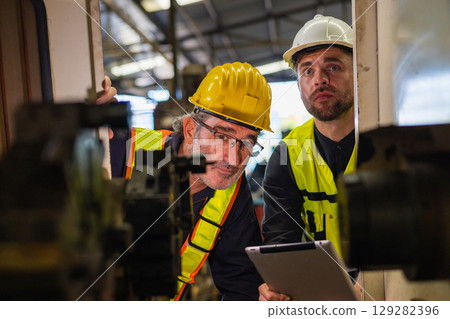 Two men in safety gear looking at a machine Two men in safety gear looking at a machine 129282396
