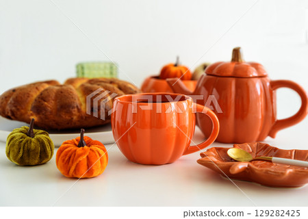 Autumnal tea set with pumpkin decor and cake on a white table. 129282425