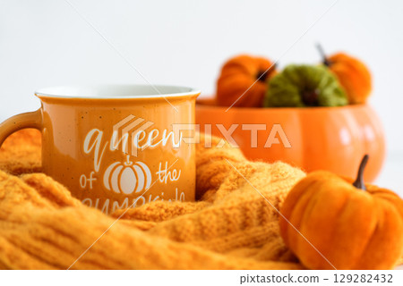 Autumnal mug with "Queen of the Pumpkins" text, surrounded by decorative pumpkins on a cozy knitted blanket. 129282432