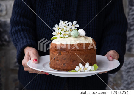 A woman holding a plate with a homemade Easter cake decorated with spring flowers and eggs. Horizontal. A woman holding a plate with a homemade Easter cake decorated with spring flowers and eggs. Horizontal. 129282541