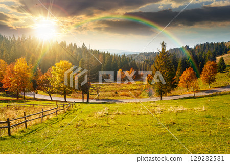 countryside mountain landscape in autumn at sunset. rural road winding through valley among field and trees on the hill. scenic vista in fall season for travel and outdoor adventure in evening light 129282581