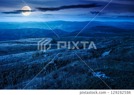 mountain landscape in summer at night. beautiful view of rolling green hills and alpine meadows in full moon light. scenery with clouds on the dark sky. scenic nature background for travel 129282586