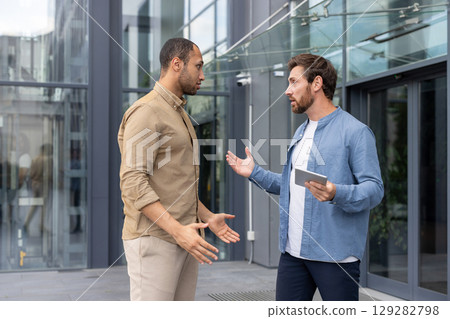 Two men engaged in a heated discussion outside a modern building, possibly a workplace conflict 129282798