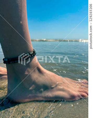 Beautiful female legs with a anklet on the beach. Sea wave washes female legs 129283166