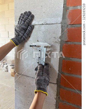 Worker's hands measure the diameter of a dowel in a wall with a caliper. Metal caliper, construction and working measuring tool. 129283210