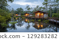 Tranquil jungle retreat with cozy wooden cabins overlooking serene waterway at dusk 129283282