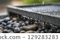Raindrops cascading over metal surface and smooth pebbles in tranquil garden scene 129283283