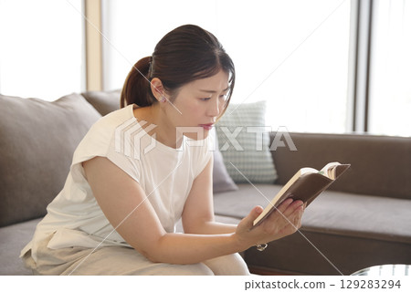 A woman who sits on a sofa and reads a book A woman who sits on a sofa and reads a book 129283294