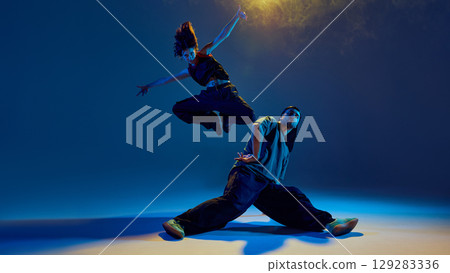 Female dancer mid-air in jump over male partner with explosive motion and focus 129283336