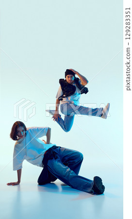 Street dancer mid-air with intense expression while partner supports pose on floor 129283351