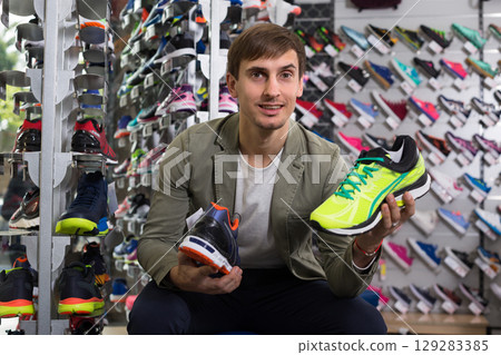 Interested man comparing two pairs of running shoes in store 129283385