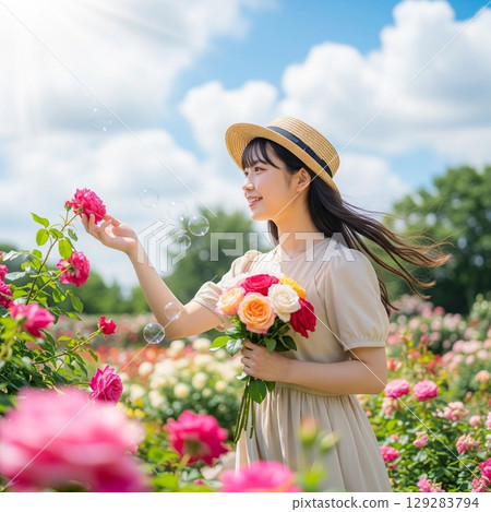 Summer portrait of a smiling woman wearing a straw hat in a colorful rose field, her long hair and ribbon swaying in the wind 129283794