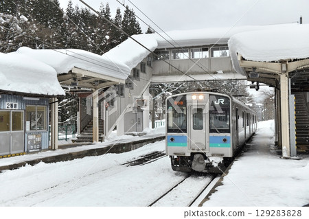 On January 2nd, snow still remains on the station building at Yanaba Station on the JR Oito Line, where an E127 series local train waits for the express train to pass. 129283828