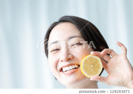 A woman with a clear face holding a lemon and showing a fresh smile. Close-up of her face. A woman with a clear face holding a lemon and showing a fresh smile. Close-up of her face. 129283871
