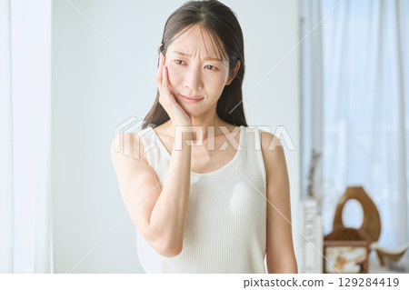 Woman suffering from toothache, holding cheek, young woman in white tank top Woman suffering from toothache, holding cheek, young woman in white tank top 129284419