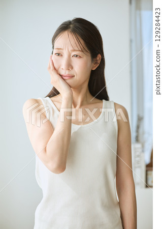 Woman suffering from toothache, holding cheek, young woman in white tank top Woman suffering from toothache, holding cheek, young woman in white tank top 129284423