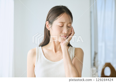 Woman suffering from toothache, holding cheek, young woman in white tank top 129284424