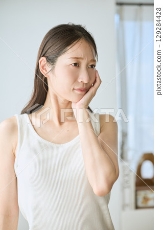 Woman suffering from toothache, holding cheek, young woman in white tank top 129284428