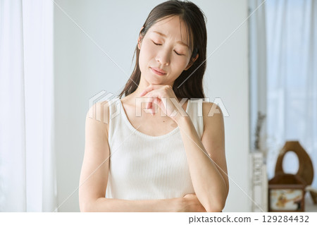A woman deep in thought, white sleeveless, natural light, worried and anxious 129284432