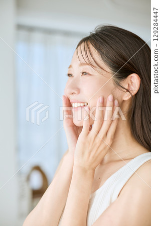A smiling woman with her hands on her skin - ideal for beauty and skincare images 129284447