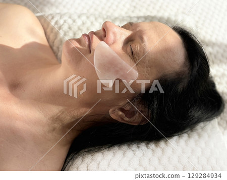 Mature woman lying on cosmetology table during professional facial massage with natural scraper. Anti aging skin care in beauty clinic. Wrinkles, skin care, beauty and wellness concept 129284934