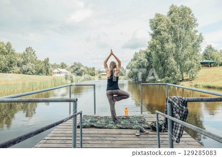 morning balance practice by the lake tree pose on wooden dock in outdoor solitude. outdoor mindfulness retreat solo yoga session with scenic water and trees 129285083