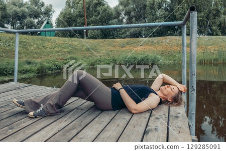 rural moment of calm rest near lake, woman lying with closed eyes, enjoying nature, concept of unplugging, nature connection, self reflection 129285091