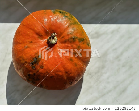 Pumpkin lying on the surface in warm sunlight. Autumn harvest and seasonal vegetables. Healthy nutrition and food concept. Halloween symbol. Close up photo Pumpkin lying on the surface in warm sunlight. Autumn harvest and seasonal vegetables. Healthy nutrition and food concept. Halloween symbol. Close up photo 129285145