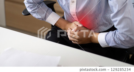 Office Syndrome: Young woman experiencing abdominal pain while seated at desk 129285234