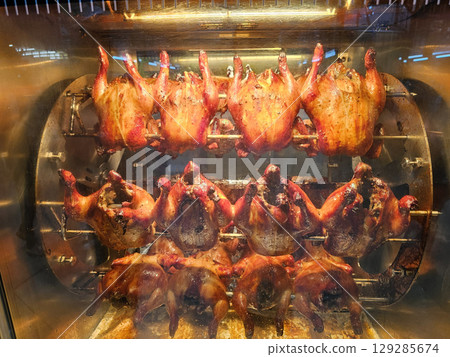 Golden brown rotisserie chickens rotating on spits inside a commercial oven or display unit. Golden brown rotisserie chickens rotating on spits inside a commercial oven or display unit. 129285674