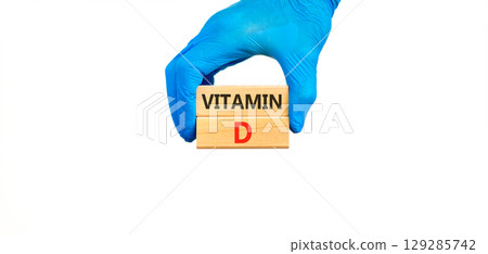 Vitamin D symbol. Concept words Vitamin D on beautiful wooden blocks. Doctor's hand in blue medical glove. Beautiful white background. Medical healthy lifestyle Vitamin D concept. 129285742