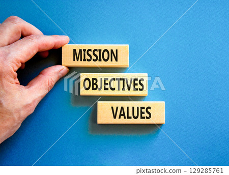 Mission objectives values symbol. Concept words Mission Objectives Values on beautiful blocks. Beautiful blue background. Businessman hand. Business mission objectives values concept. Copy space. 129285761