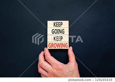 Keep going and growing symbol. Concept words phrase Keep going keep growing on beautiful wooden blocks. Beautiful black background. Businessman's hand. Business Keep going growing concept. Copy space. 129285819