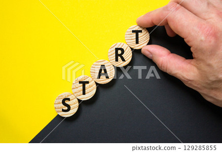 Start symbol. Concept word Start on beautiful wooden circles. Beautiful yellow and black background. Businessman hand. Business lifestyle start concept. Copy space. Start symbol. Concept word Start on beautiful wooden circles. Beautiful yellow and black background. Businessman hand. Business lifestyle start concept. Copy space. 129285855