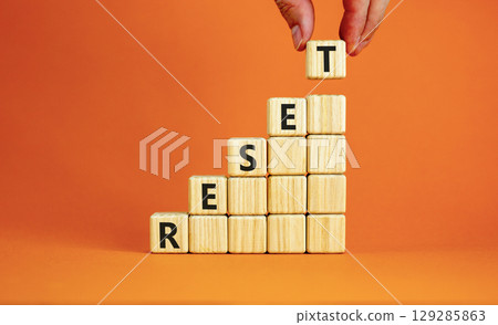 Reset symbol. Concept word Reset on beautiful wooden blocks. Beautiful orange table orange background. Businessman hand. Business lifestyle reset concept. Copy space. Reset symbol. Concept word Reset on beautiful wooden blocks. Beautiful orange table orange background. Businessman hand. Business lifestyle reset concept. Copy space. 129285863