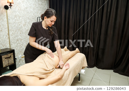Female Massage Therapist Addressing Cellulite Issues on Women's Thighs, Legs, and Buttocks with Expertise 129286043