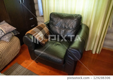 Black leather armchair with warm plaid in cozy wooden room 129286306