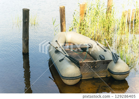 Inflatable boat moored near wooden pier on calm lake Inflatable boat moored near wooden pier on calm lake 129286405
